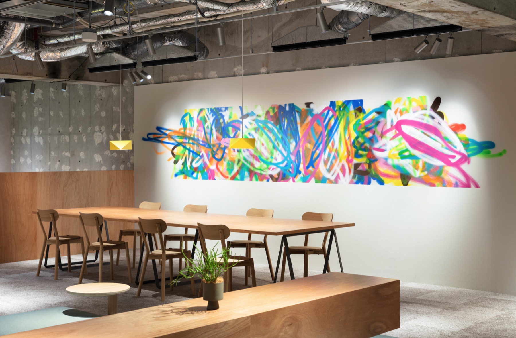 A collaborative workshop space with a long shared table and a large colourful mural
